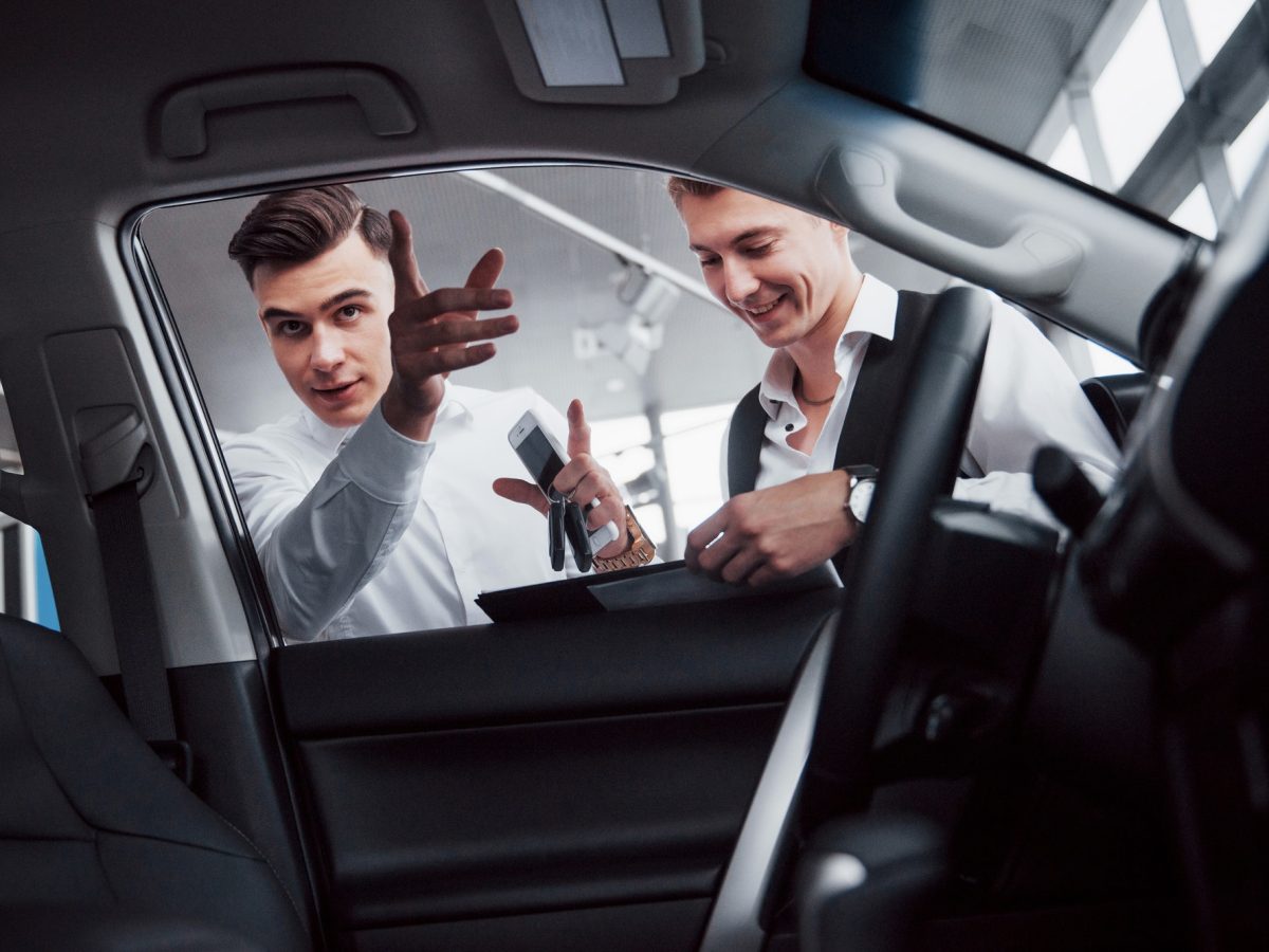 Two men stand in the showroom against cars. Sales manager in a suit that sells a car to a customer